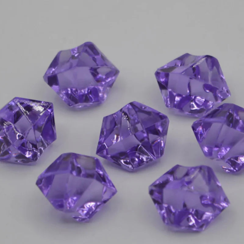 A collection of purple acrylic crystal decorations for parties scattered on a light gray surface.
