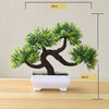 Artificial bonsai tree in a white pot with green foliage displayed on a wooden surface.