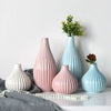 A grouping of elegant ceramic flower vases in pink and blue tones on a white surface.