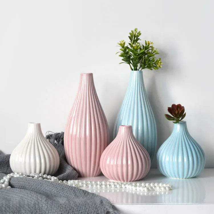 A grouping of elegant ceramic flower vases in pink and blue tones on a white surface.