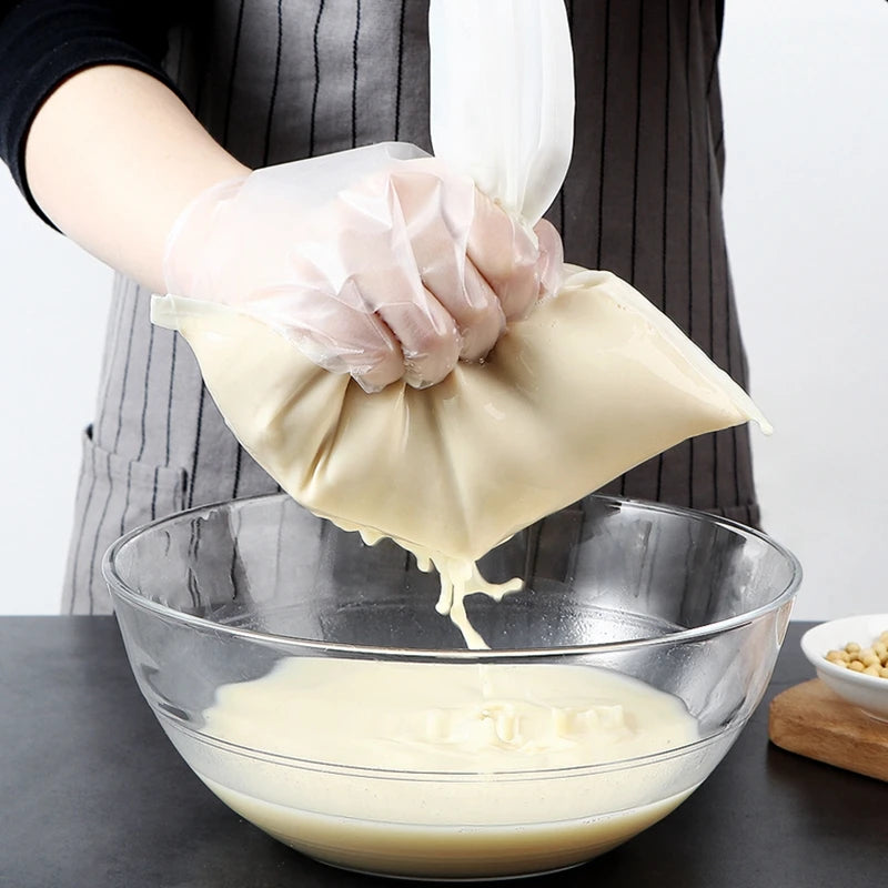 A hand wearing a white glove is squeezing a clear nylon filter bag filled with light-colored liquid into a glass bowl.