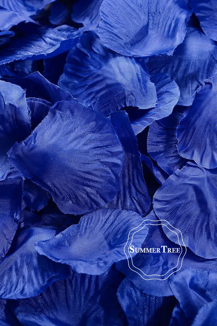 A close-up of deep blue silk rose petals scattered on a dark surface.