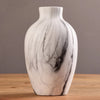 A white ceramic vase with black marble veining sits on a wooden surface.