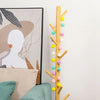 A vertical garland of colorful felt balls in yellow, pink, green, and white strung on a wooden branch.
