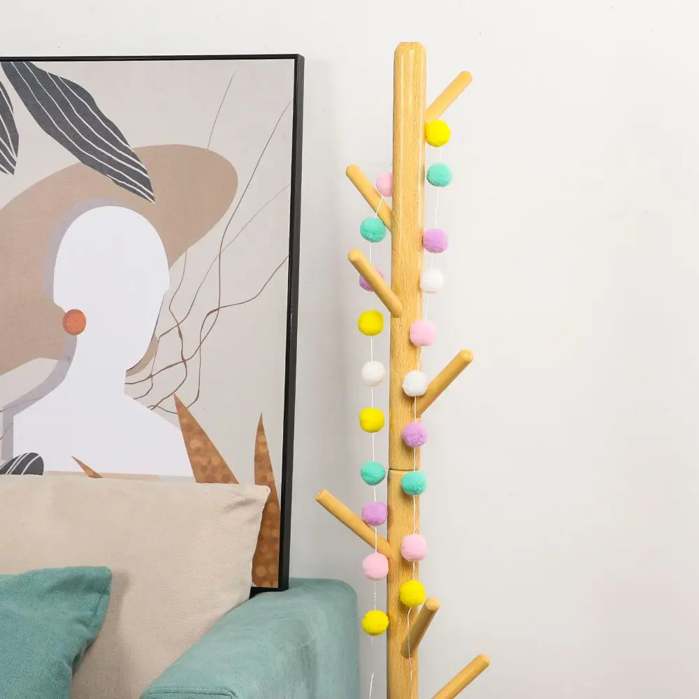 A vertical garland of colorful felt balls in yellow, pink, green, and white strung on a wooden branch.