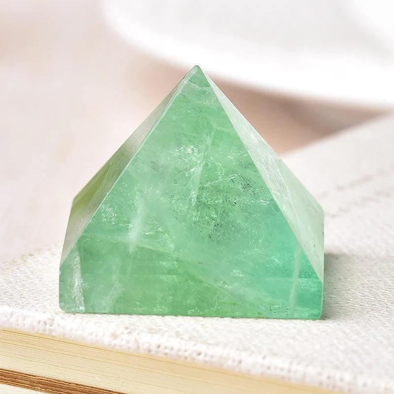 Cristal piramidal de fluorita verde natural sobre una superficie blanca texturizada.