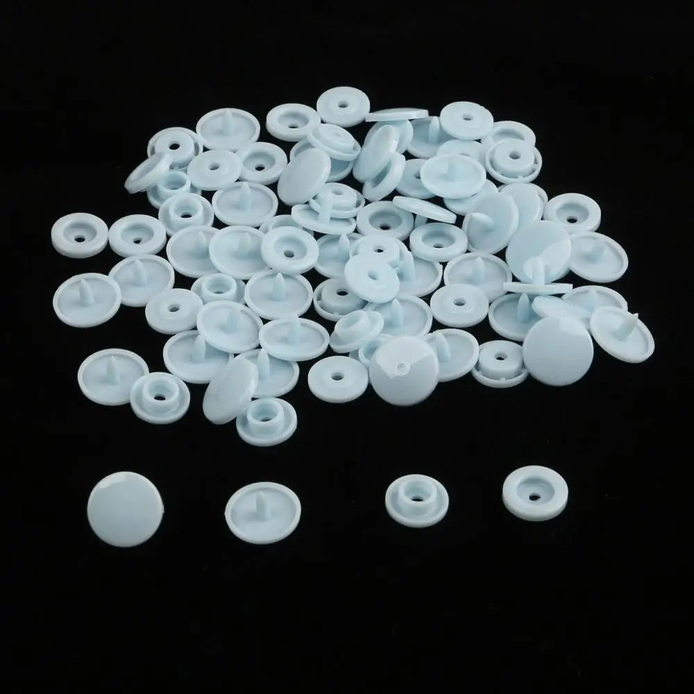 A pile of assorted white snap buttons, measuring 12mm and 10.5mm, scattered on a black surface.