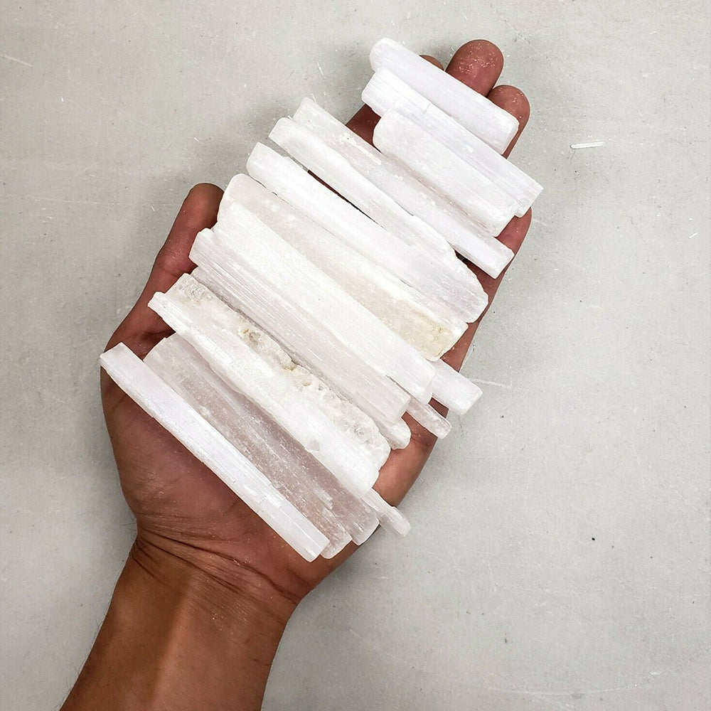 A hand holds several white natural selenite crystal wands for healing and crafting.
