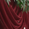 Deep burgundy chiffon fabric draped elegantly, used as a wedding arch backdrop.