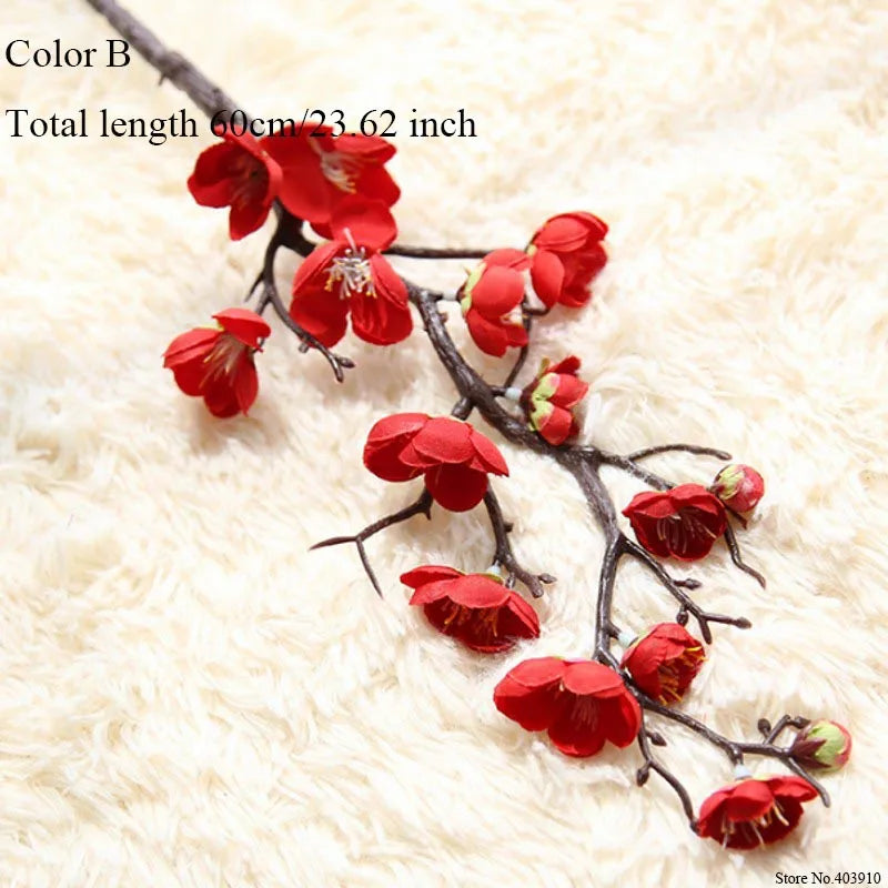 A branch of artificial silk cherry blossoms in red on a white fluffy background.