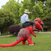 A person wearing a red and black T-Rex inflatable costume is walking across a green lawn.