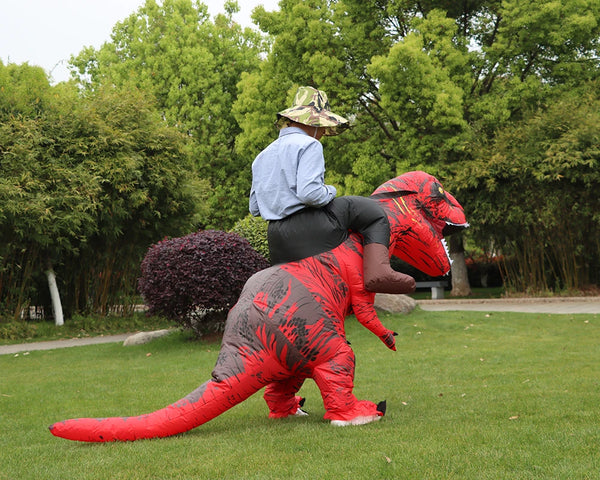 A person wearing a red and black T-Rex inflatable costume is walking across a green lawn.