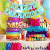 Una colorida celebración de cumpleaños con pastel de varios niveles, globos y un letrero decorativo.