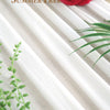 A close-up of elegant cream and white chiffon fabric draped in vertical stripes with a red rose and green foliage.