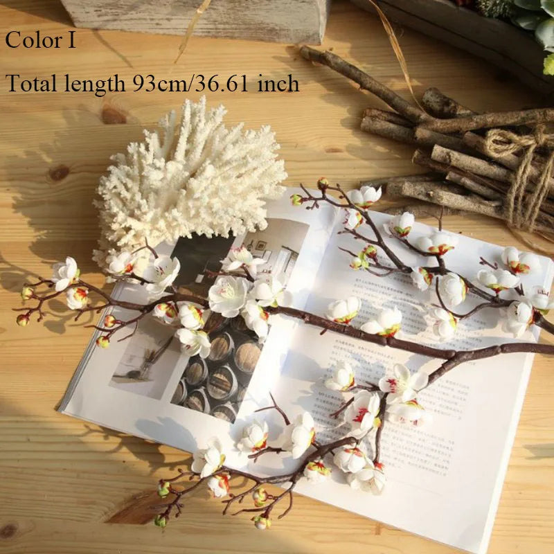 Artificial silk cherry blossom branches with white flowers displayed on a wooden surface.