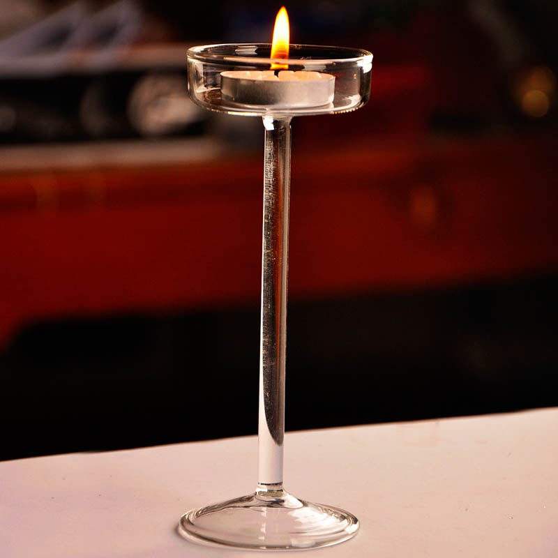 Elegant glass candle holder with a lit candle on a clear stem and base.