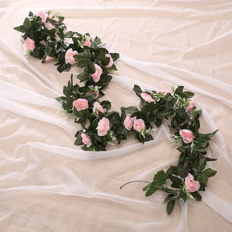 A lush garland of pink and green silk roses and foliage draped across sheer fabric.