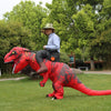 A person is posing with a large, red inflatable T-Rex costume in a grassy outdoor setting.