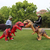 Two people in inflatable T-Rex costumes posing outdoors in a grassy park.