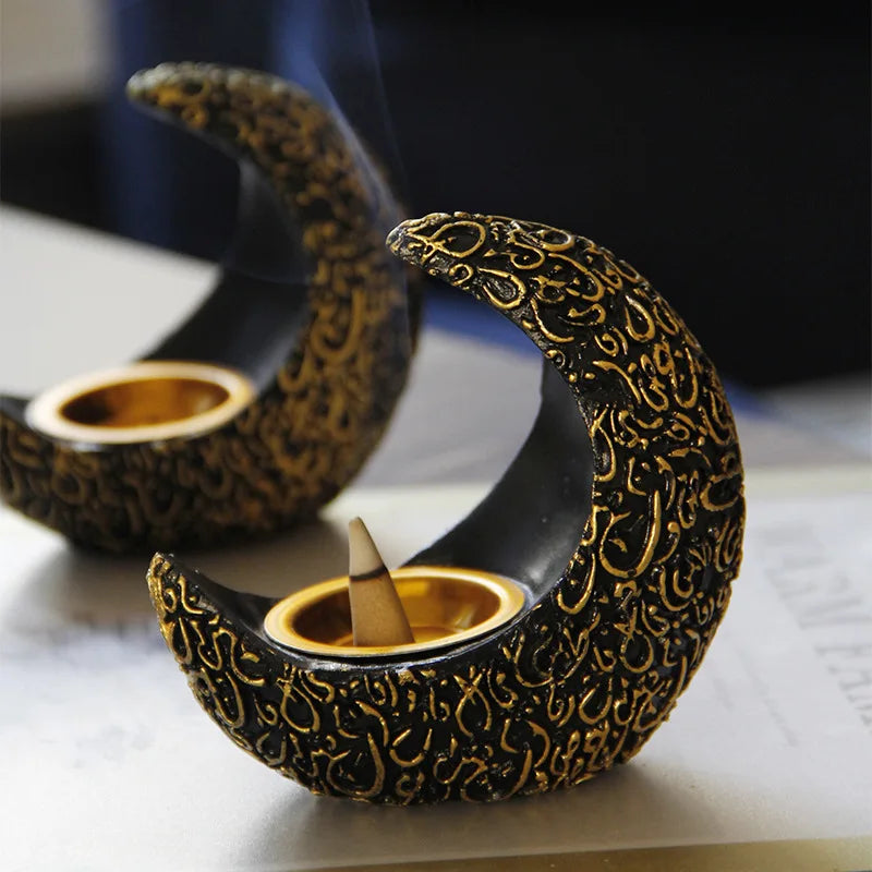 A black resin crescent incense burner with gold detailing is shown smoking on a white surface.