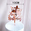 Rose gold acrylic happy birthday cake topper with a crown and text on a white cake pedestal