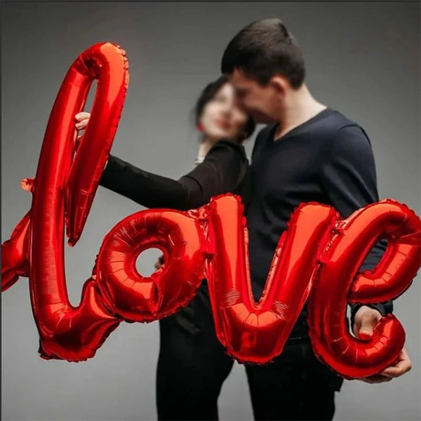 Una pareja sostiene un gran globo de aluminio rojo con forma de la palabra AMOR.