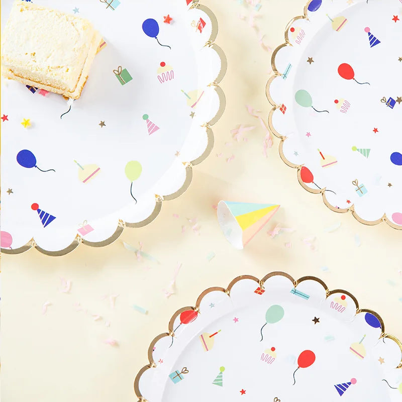 A collection of white disposable paper party plates with gold trim and colorful confetti decorations.