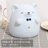 A white cartoon bear-shaped piggy bank with black eyes and a blue bow, sitting on a gray checkered surface.