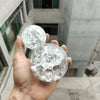 A hand holds a clear, spherical crystal ball water feature ornament against a blurred building background.