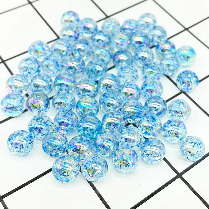 A pile of clear blue iridescent acrylic round beads for jewelry making scattered on a grid background.