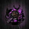 A black silhouette of a deer head and pine trees forms the face of a wall clock with a purple glow.
