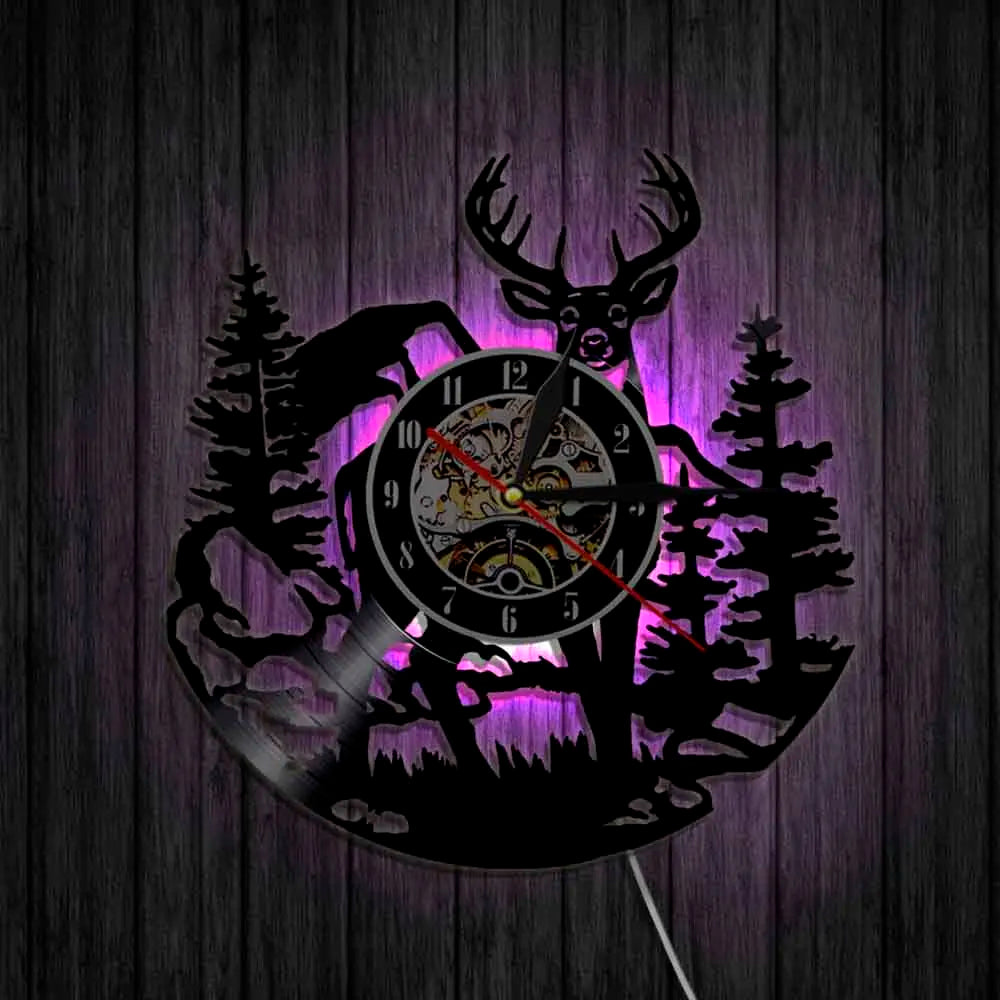 A black silhouette of a deer head and pine trees forms the face of a wall clock with a purple glow.
