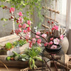 Pink artificial silk cherry blossom branches with green leaves displayed in a rustic decor setting