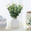 A vase filled with green silk eucalyptus leaf stems used for home and event decor.