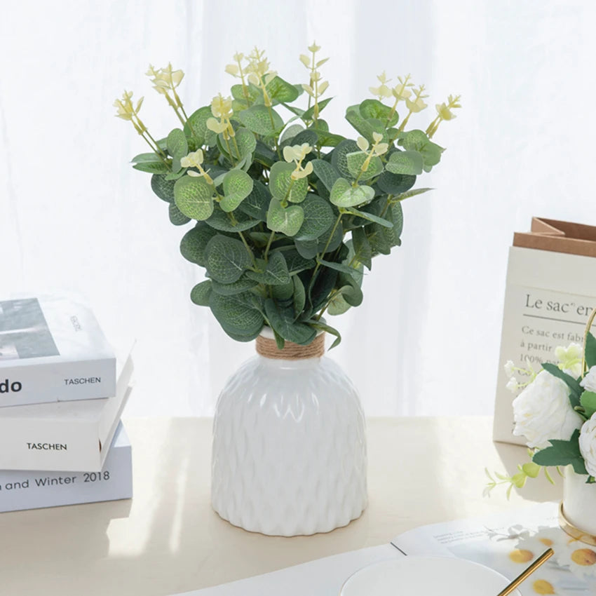 A vase filled with green silk eucalyptus leaf stems used for home and event decor.