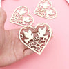A hand holds a set of ten wooden heart-shaped hanging ornaments featuring delicate bird cutouts.