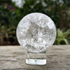 A clear, spherical crystal ball water feature ornament resting on a glass stand.