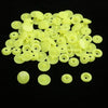 A pile of assorted light yellow snap buttons, measuring 12mm and 10.5mm, scattered on a black surface.