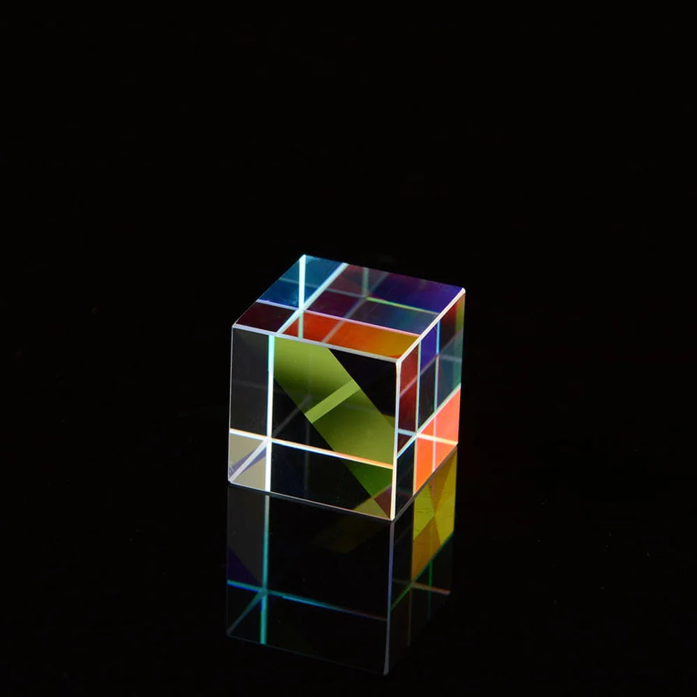 A transparent cube filled with colorful optical glass prisms reflecting light on a dark surface.