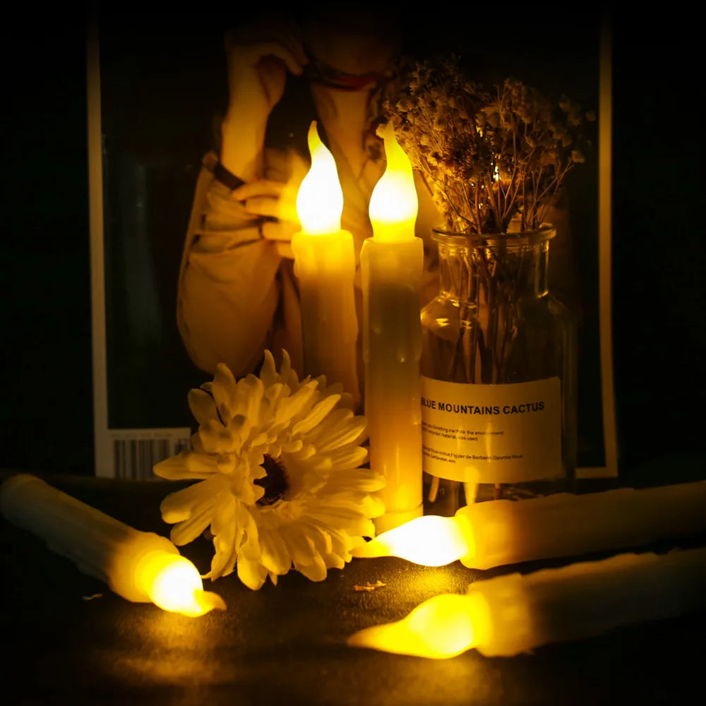 A collection of glowing white LED taper candles in a glass jar and several unlit candles on a dark surface.