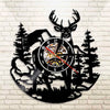 A black silhouette wall clock featuring a deer head and pine trees in a woodland theme.