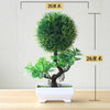 Artificial bonsai tree in a white pot with green foliage, displayed on a wooden surface.