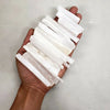 A hand holds several white natural selenite crystal wands for healing and crafting.