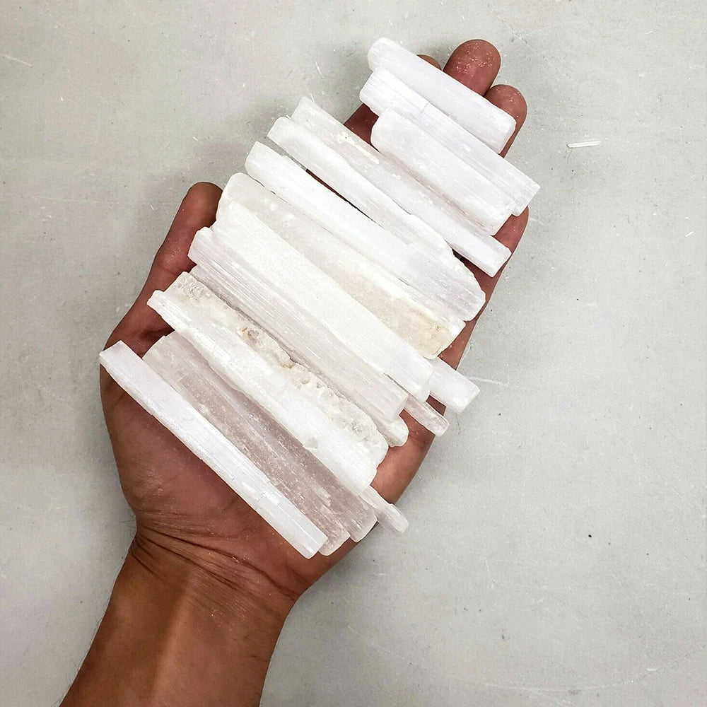 A hand holds several white natural selenite crystal wands for healing and crafting.