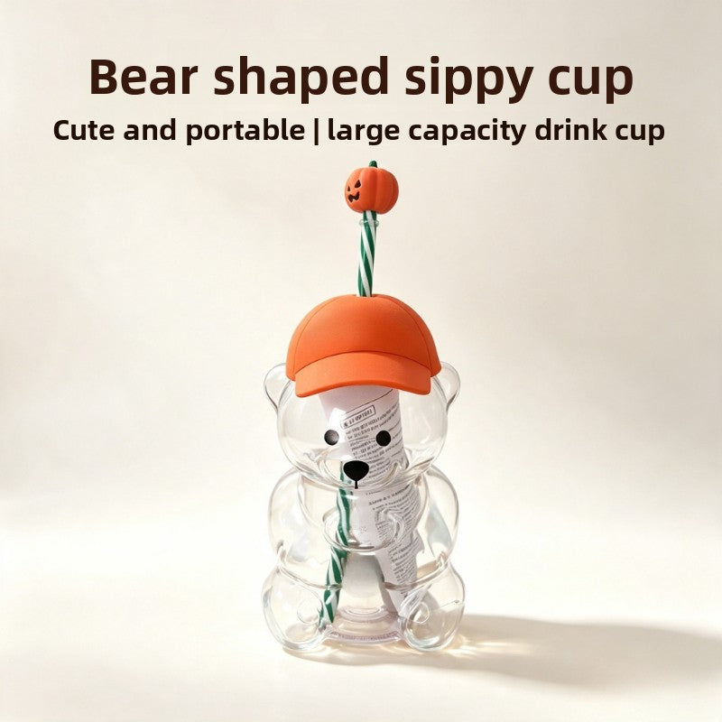 A bear-shaped sippy cup with an orange body and a green striped straw, sitting on a light surface.
