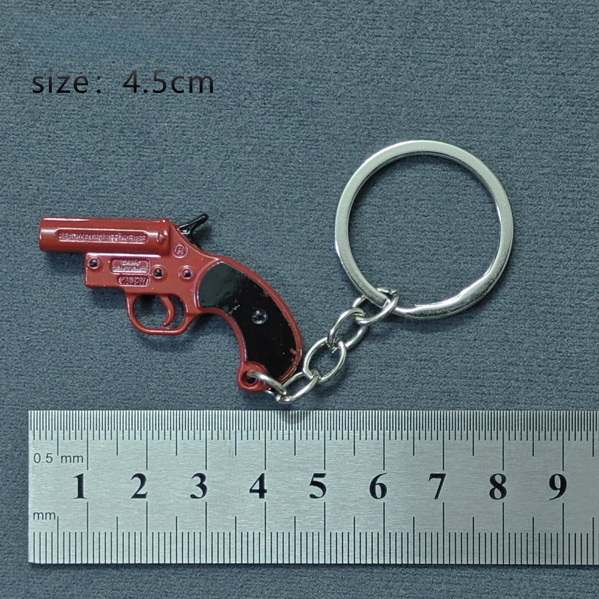 A red miniature alloy gun model keychain with a silver split ring attached, shown next to a ruler.