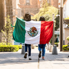 A person holds a large Mexican flag outdoors on a sunny day.