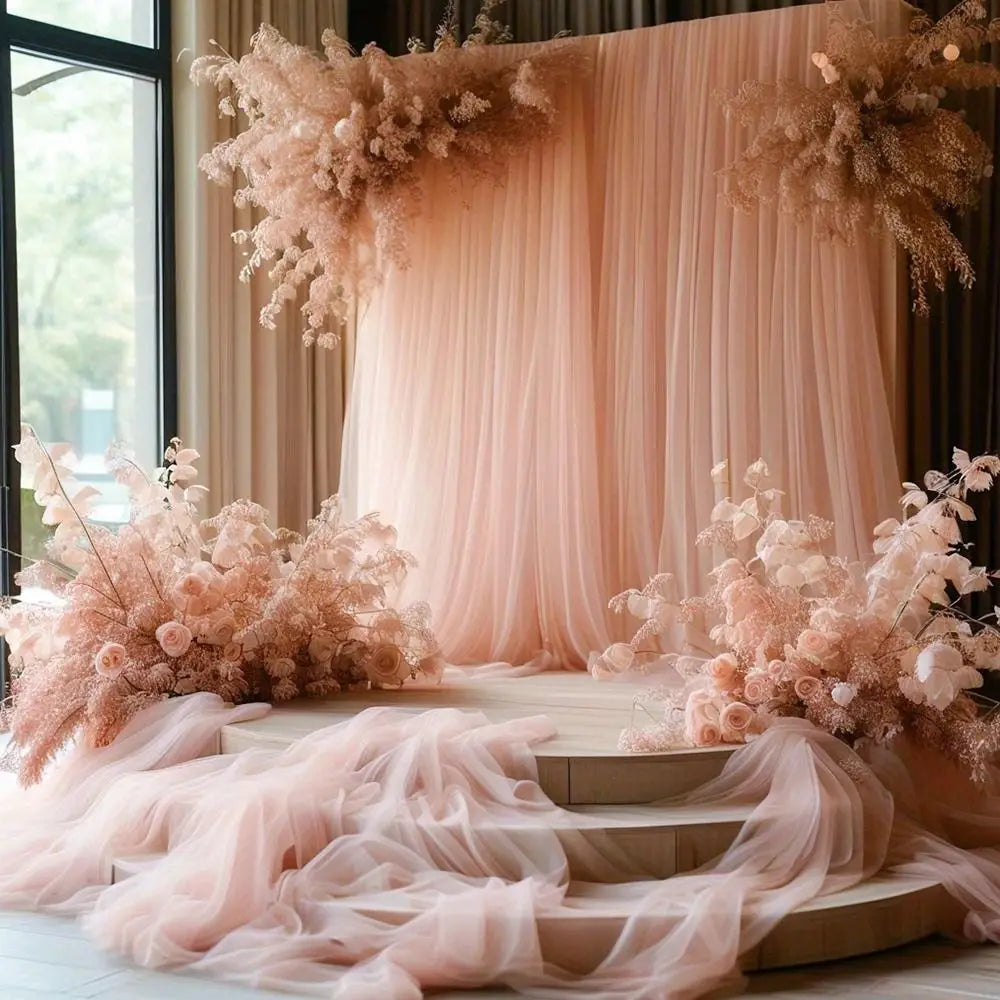 Soft pink sheer tulle fabric draped behind floral arrangements on a wooden stage.
