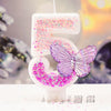 A white birthday candle shaped like the number 5 decorated with pink and purple glitter and a purple butterfly