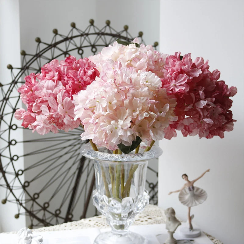 A bouquet of pink and white silk hydrangea stems with vintage burnt edge petals displayed on a glass vase.